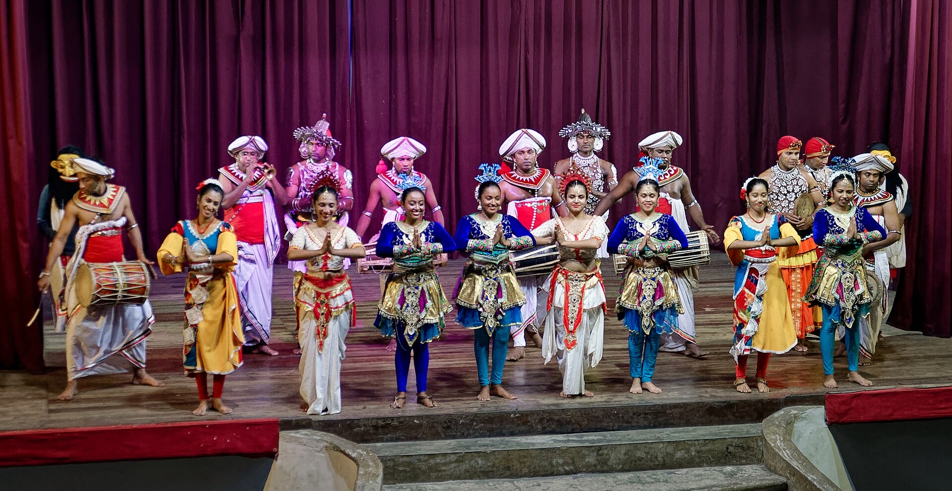 A troupe of Kandyan dancers and drummers in red and silver costumes on stage