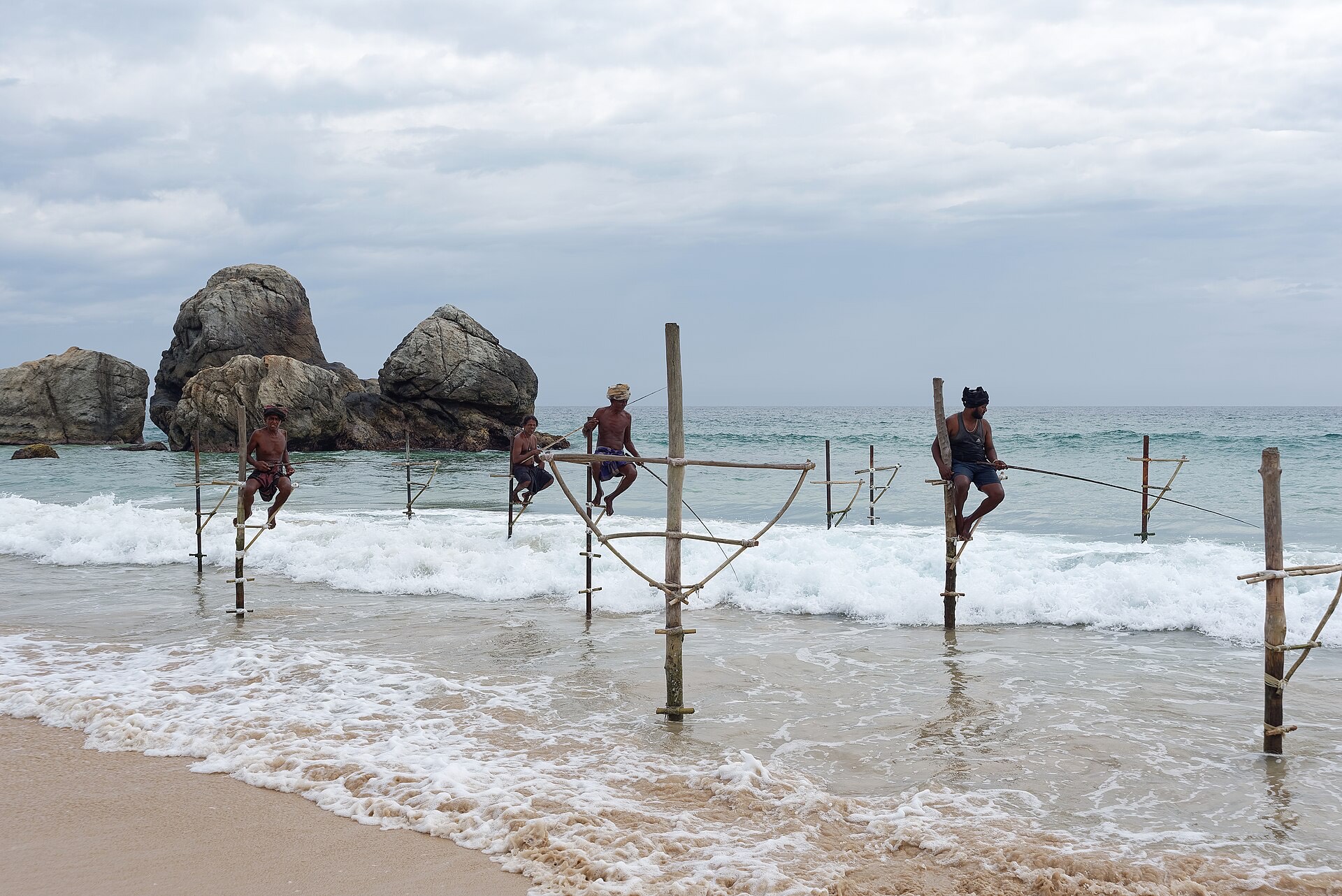 Fishermen perched on wooden stilts in the surf near Galle